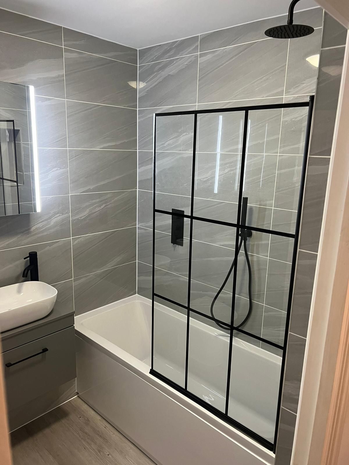 Bath with a black-framed shower screen and grey tiling