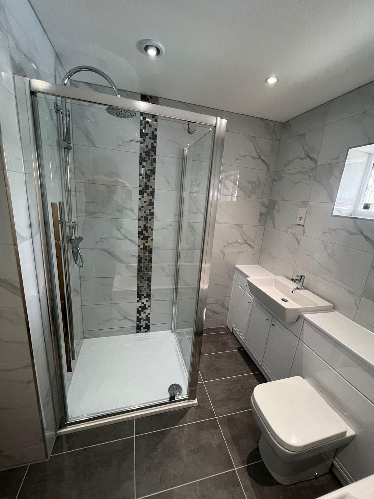 Marble-effect shower room with a glass enclosure and mosaic band