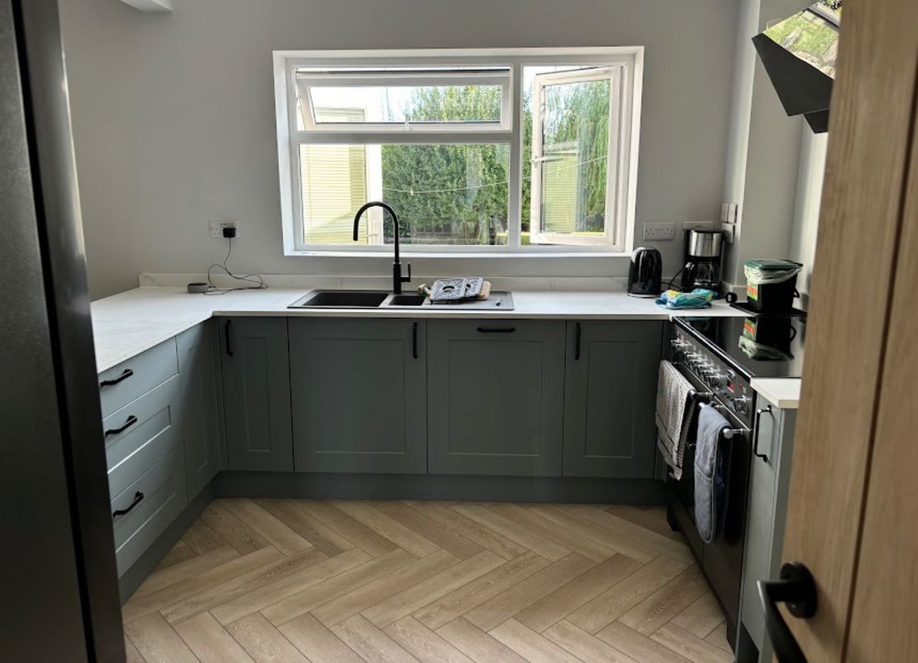 Green shaker kitchen with herringbone flooring and a black mixer tap